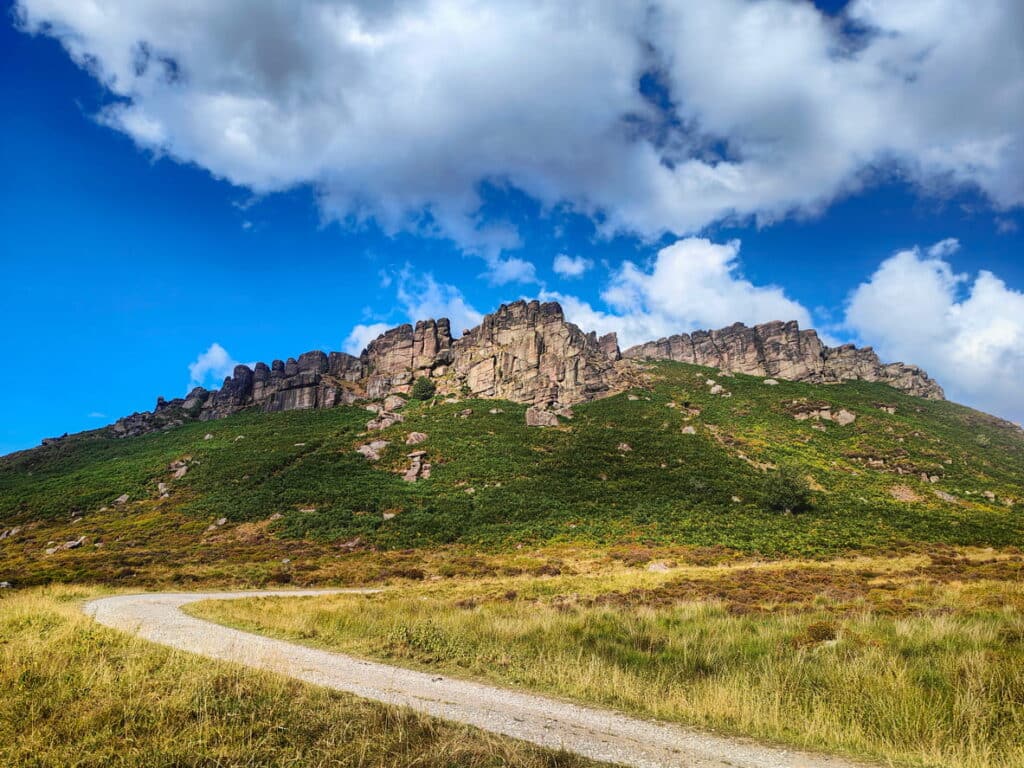 The Roaches rocky ridge in the Staffordshire Peak District with a winding footpath, moorland and blue sky