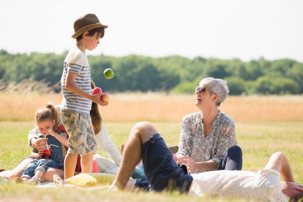 Three generations of a family enjoying a picnic on a blanket in a sunny grassy field in Staffordshire